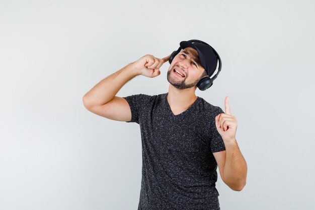 Varón joven en camiseta y gorra escuchando música con el dedo hacia arriba y mirando encantado