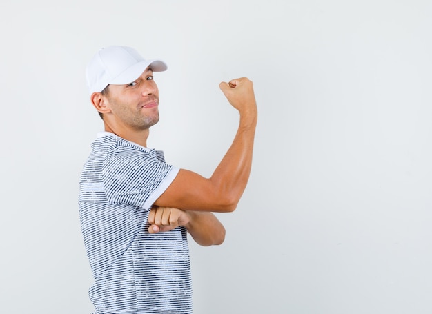 Foto gratuita varón joven en camiseta y gorra mostrando los músculos del brazo y mirando contento.