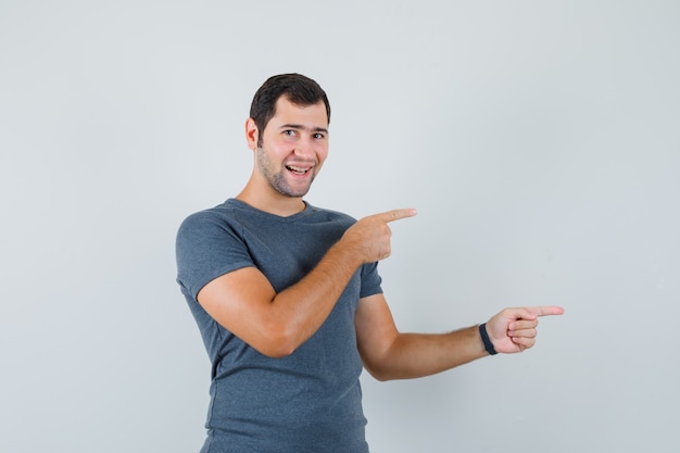 Varón joven en camiseta gris apuntando hacia el lado y mirando alegre