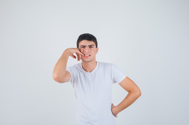 Foto gratuita varón joven en camiseta mordiéndose las uñas y mirando pensativo, vista frontal.