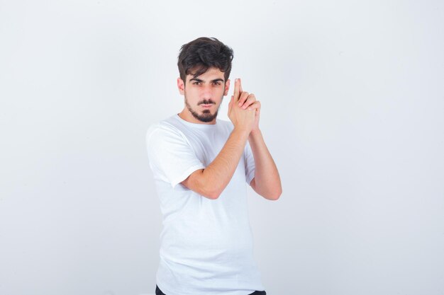 Varón joven en camiseta mostrando gesto de pistola y mirando confiado, vista frontal.