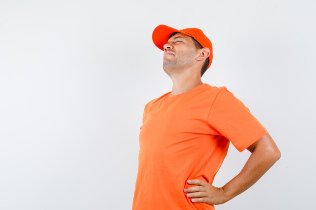 Varón joven en camiseta naranja y gorra con dolor de espalda y aspecto cansado