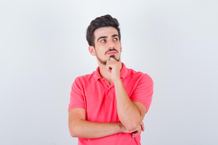 Foto gratuito varón joven en camiseta de pie en pose de pensamiento y mirando sensible, vista frontal.