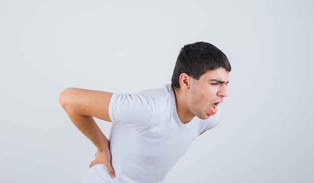 Varón joven en camiseta que sufre de dolor lumbar y se ve mal, vista frontal.