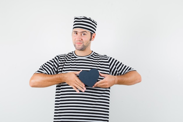 Foto gratuita varón joven en camiseta a rayas, gorra con mini caja de regalo, vista frontal.