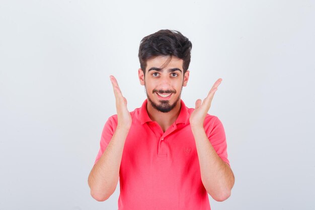 Varón joven en camiseta rosa cogidos de la mano cerca de la cabeza y mirando alegre, vista frontal.