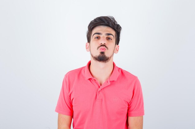 Varón joven en camiseta rosa haciendo pucheros con los labios y luciendo elegante, vista frontal.