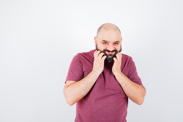 Varón joven en camiseta rosa rascándose la barba, vista frontal.