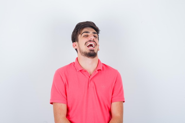 Varón joven en camiseta rosa riendo y mirando confiado, vista frontal.