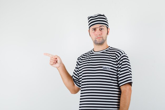 Varón joven en camiseta, sombrero apuntando hacia el lado izquierdo y mirando vacilante, vista frontal.