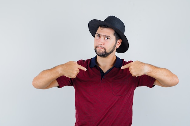 Foto gratuita varón joven en camiseta, sombrero apuntando a sí mismo y mirando serio, vista frontal.