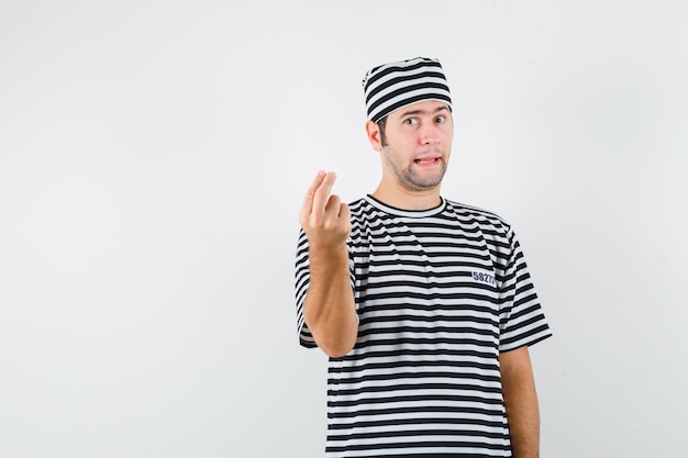Foto gratuita varón joven en camiseta, sombrero haciendo gesto italiano, disgustado con pregunta tonta, vista frontal.