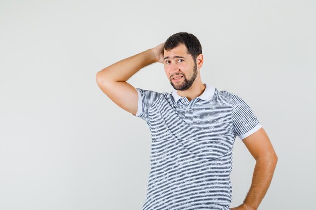 Varón joven en camiseta sosteniendo la mano en el cuello y mirando elegante, vista frontal.