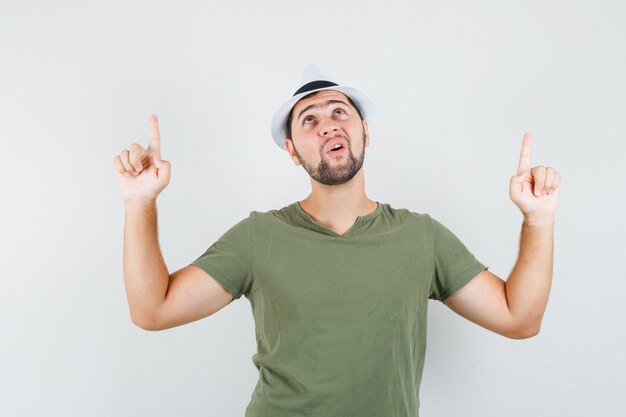 Varón joven en camiseta verde y sombrero apuntando hacia arriba y mirando agradecido