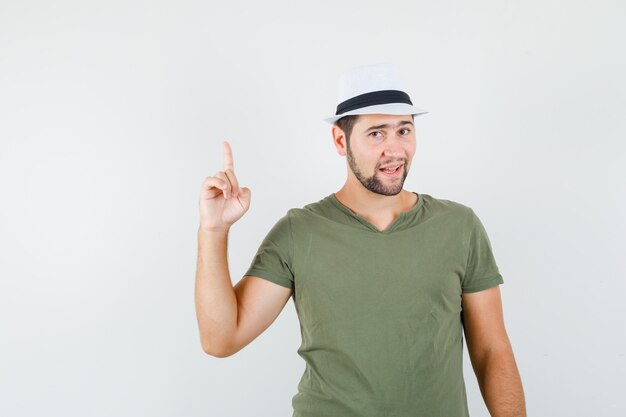 Varón joven en camiseta verde y sombrero apuntando hacia arriba y mirando confiado