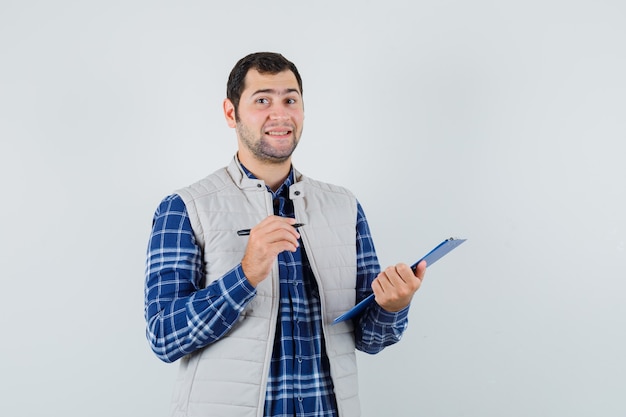 Varón joven escribiendo algo en camisa, chaqueta y mirando complacido. vista frontal.