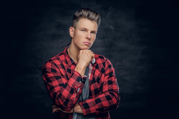 Varón joven con estilo pensativo en una camisa roja sobre fondo gris.