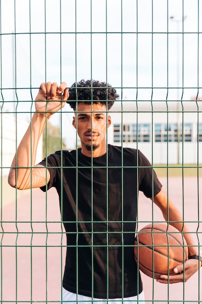 Foto gratuita varón joven étnico con baloncesto detrás de la cerca