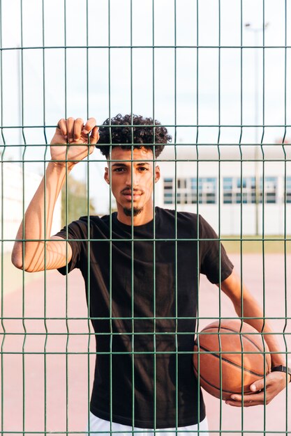 Varón joven étnico con baloncesto detrás de la cerca