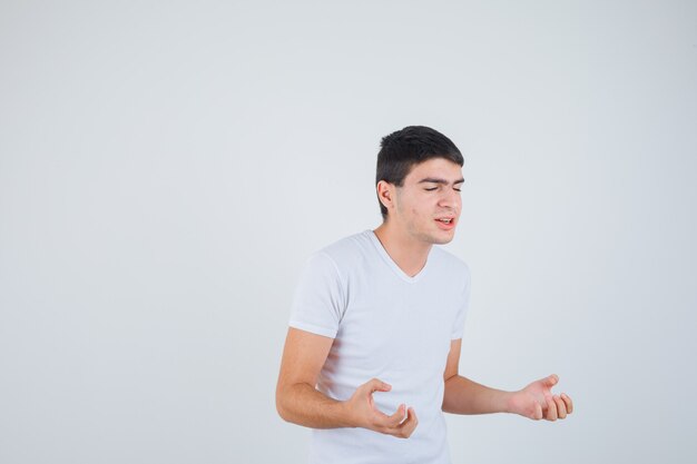 Varón joven fingiendo atrapar algo en camiseta y mirando feliz. vista frontal.