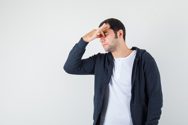 Varón joven frotándose los ojos y la nariz en camiseta, chaqueta y aspecto cansado. vista frontal.