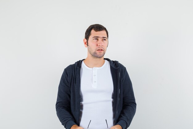 Varón joven con gafas en camiseta, chaqueta y mirando pensativo, vista frontal.