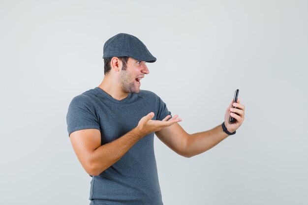 Varón joven en gorra de camiseta hablando por video chat y mirando asombrado