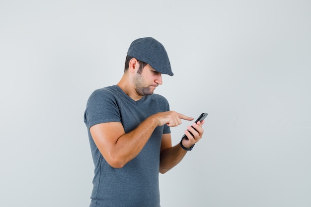 Varón joven en gorra de camiseta con teléfono móvil y mirando ocupado