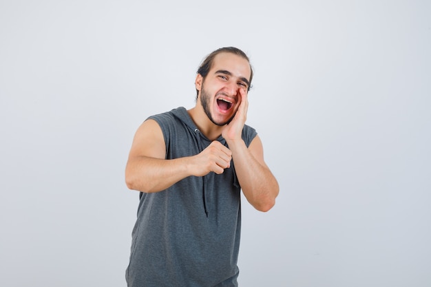 Varón joven gritando algo mientras levanta el puño cerrado en una sudadera con capucha sin mangas y parece feliz, vista frontal.