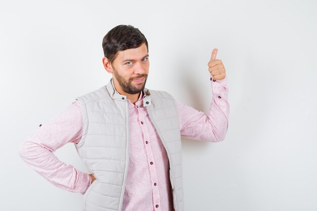 Varón joven guapo en camisa, chaleco mostrando el pulgar hacia arriba y mirando complacido, vista frontal.