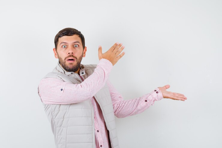 Foto gratuito varón joven guapo fingiendo mostrar algo en camisa, chaleco y mirando sorprendido, vista frontal.