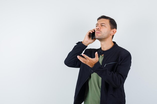 Varón joven hablando por teléfono móvil en camiseta, vista frontal de la chaqueta.