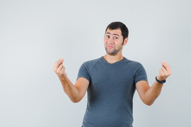 Varón joven haciendo gesto de dinero en camiseta gris