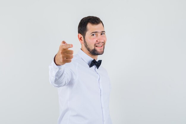 Varón joven invitando a venir con camisa blanca y mirando contento, vista frontal.