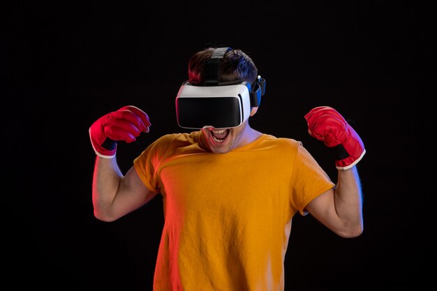 Varón joven jugando realidad virtual en guantes de mma en superficie oscura