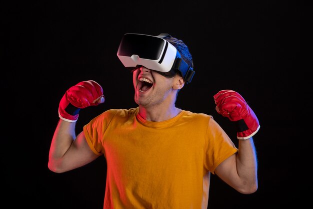 Varón joven jugando realidad virtual en guantes de mma en superficie oscura