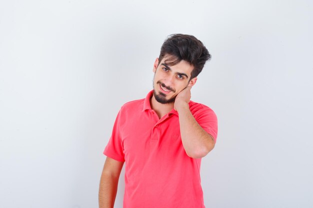 Varón joven con la mano en el cuello en camiseta y mirando feliz, vista frontal.