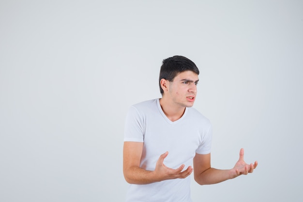 Varón joven manteniendo las manos para atrapar algo en la camiseta y mirando serio. vista frontal.