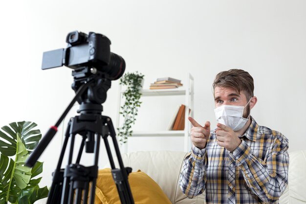 Varón joven con mascarilla grabando video en casa