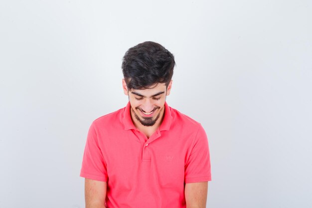 Varón joven mirando hacia abajo en camiseta rosa y mirando esperanzado, vista frontal.