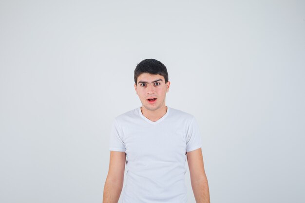 Varón joven mirando a la cámara en camiseta y mirando perplejo, vista frontal.