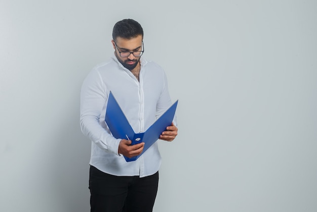 Varón joven mirando en carpeta con camisa blanca, pantalón y guapo