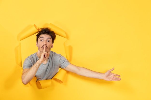 Varón joven mirando desde el fondo de papel amarillo rasgado chico facial venta interior