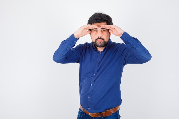 Foto gratuita varón joven mirando con las manos sobre la cabeza en camisa azul y mirando enfocado, vista frontal.