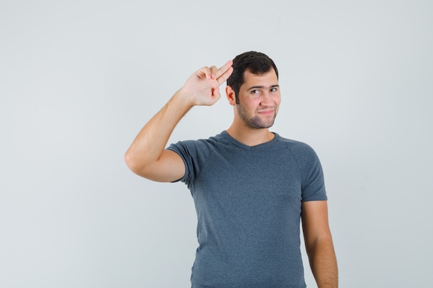 Varón joven mostrando gesto de saludo en camiseta gris y mirando confiado