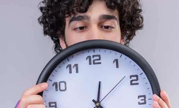 Varón joven pelo rizado aislado camisa colorida escondido detrás del reloj de cerca