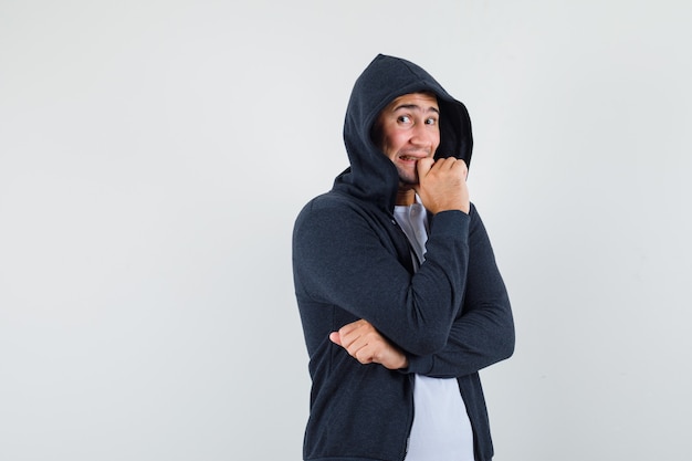 Varón joven de pie en pose de pensamiento en camiseta, chaqueta y mirando emocionado, vista frontal.