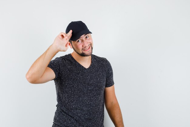 Varón joven posando con dos dedos a la cabeza en camiseta y gorra y luciendo bien