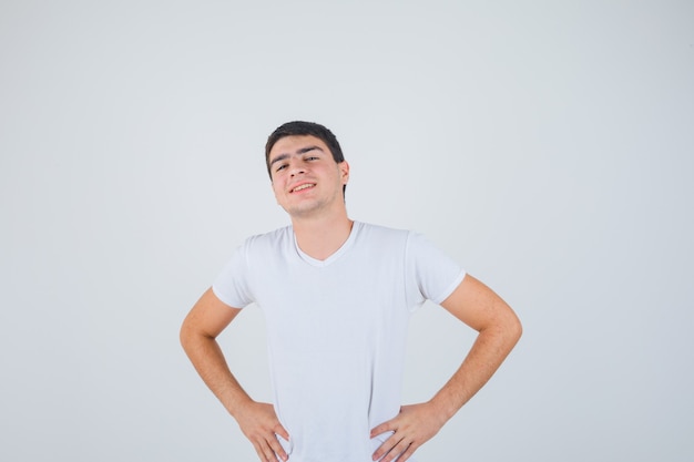 Varón joven posando con las manos en la cintura en camiseta y mirando alegre, vista frontal.