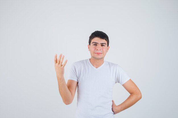 Varón joven posando mientras mira a la cámara en camiseta y parece complacido. vista frontal.